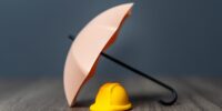 A yellow hard hat and umbrella. Worker insurance, safety first concept.