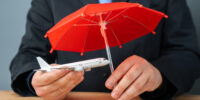 Businessman holding a plane under a red umbrella. Passenger and flight insurance. Technical support, aircraft leasing. Safety and security.
