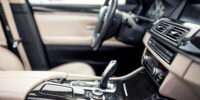 Modern beige and black interior of modern car, close-up details of automatic transmission and gear stick against steering wheel background and dashboard